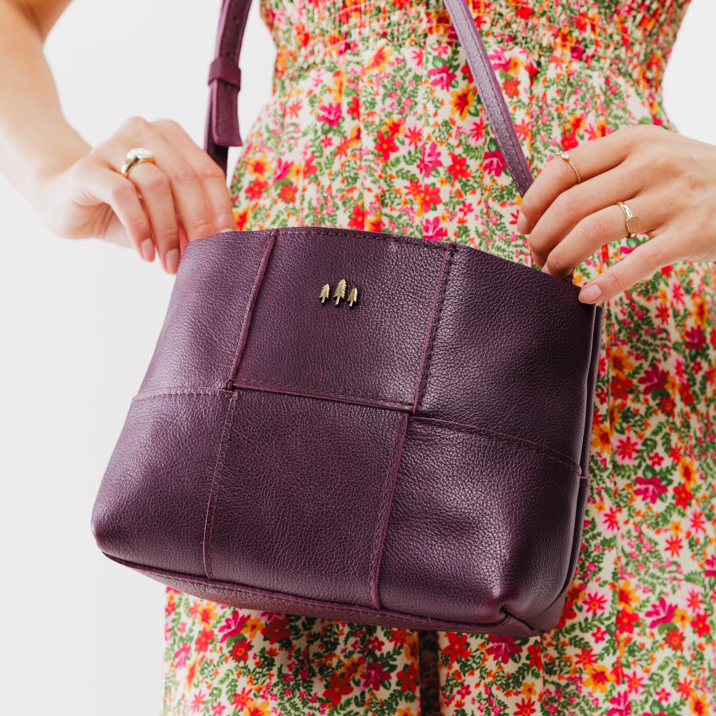 Plum*Small | Model carrying structured woven leather bag with three metal tree emblems and crossbody strap