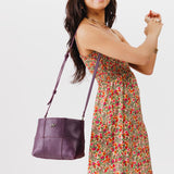 Plum Small | Model carrying structured woven leather bag with three metal tree emblems and crossbody strap