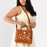 Folklore Honey Large | Model wearing mid-size tote purse with embroidered flower design, structured leather handles, and crossbody strap