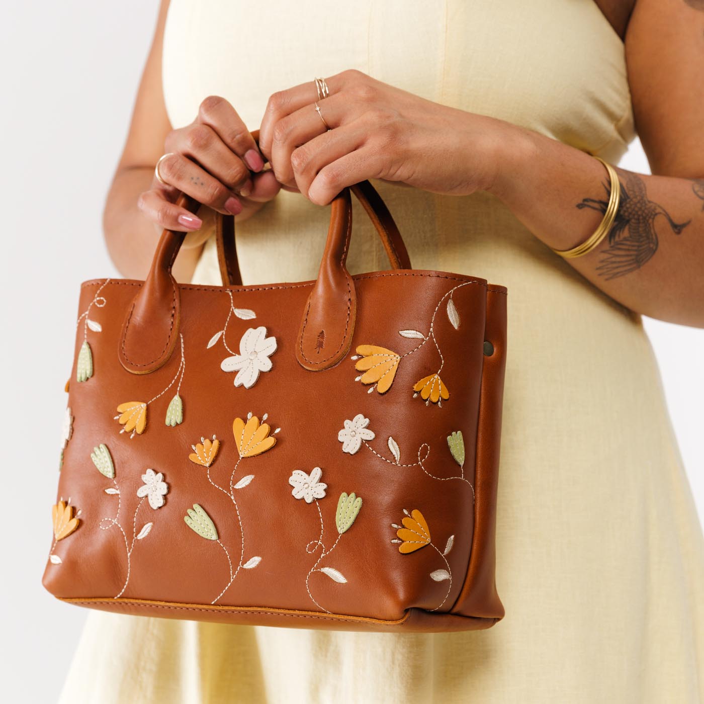 Folklore Honey*Large  | Model holding mid-size tote purse with embroidered flower design, structured leather handles, and crossbody strap