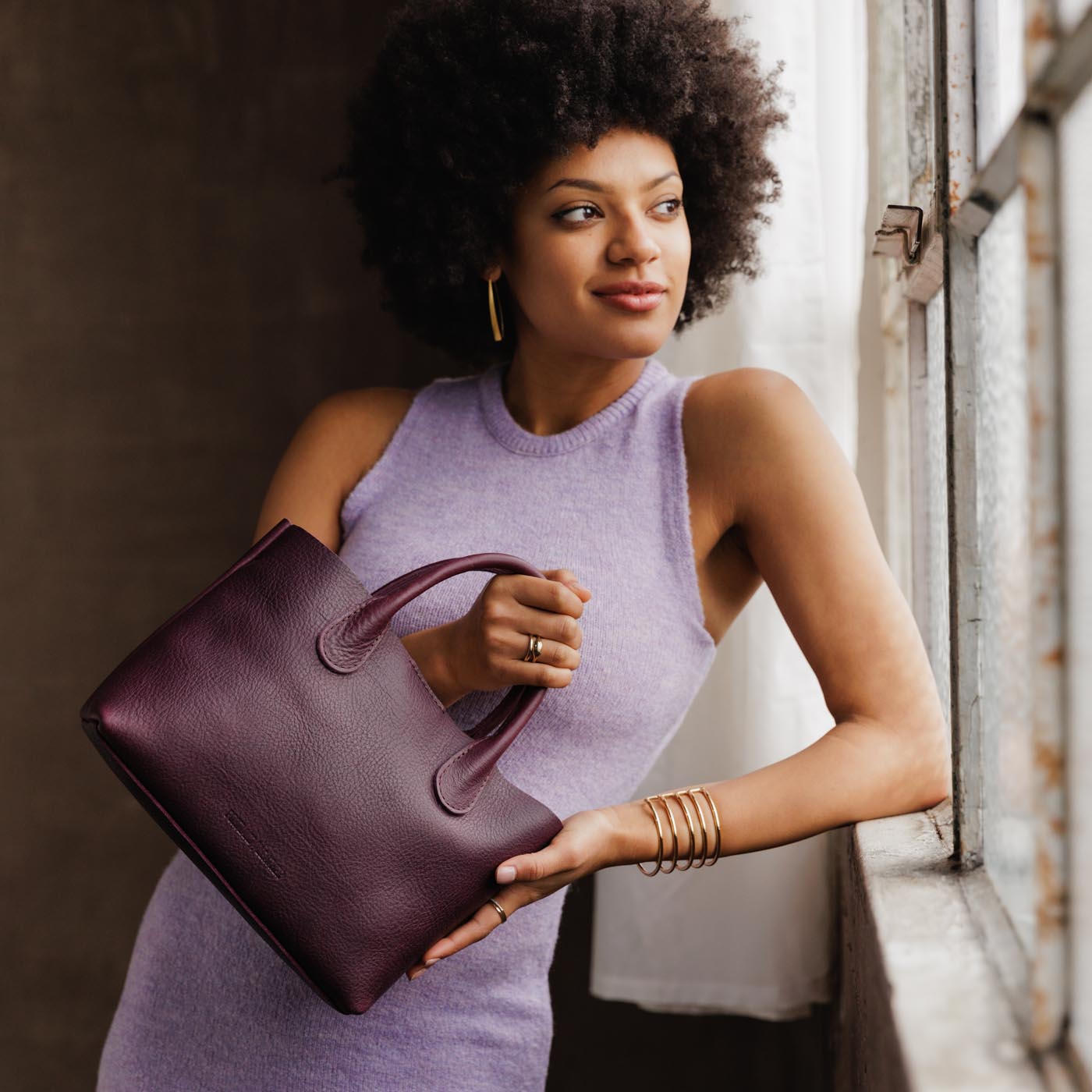 Plum*Large | Model holding mid-size tote purse with  structured leather handles and crossbody strap