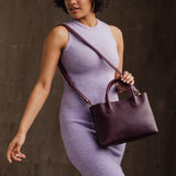 Plum Large | Model holding mid-size tote purse with  structured leather handles and crossbody strap