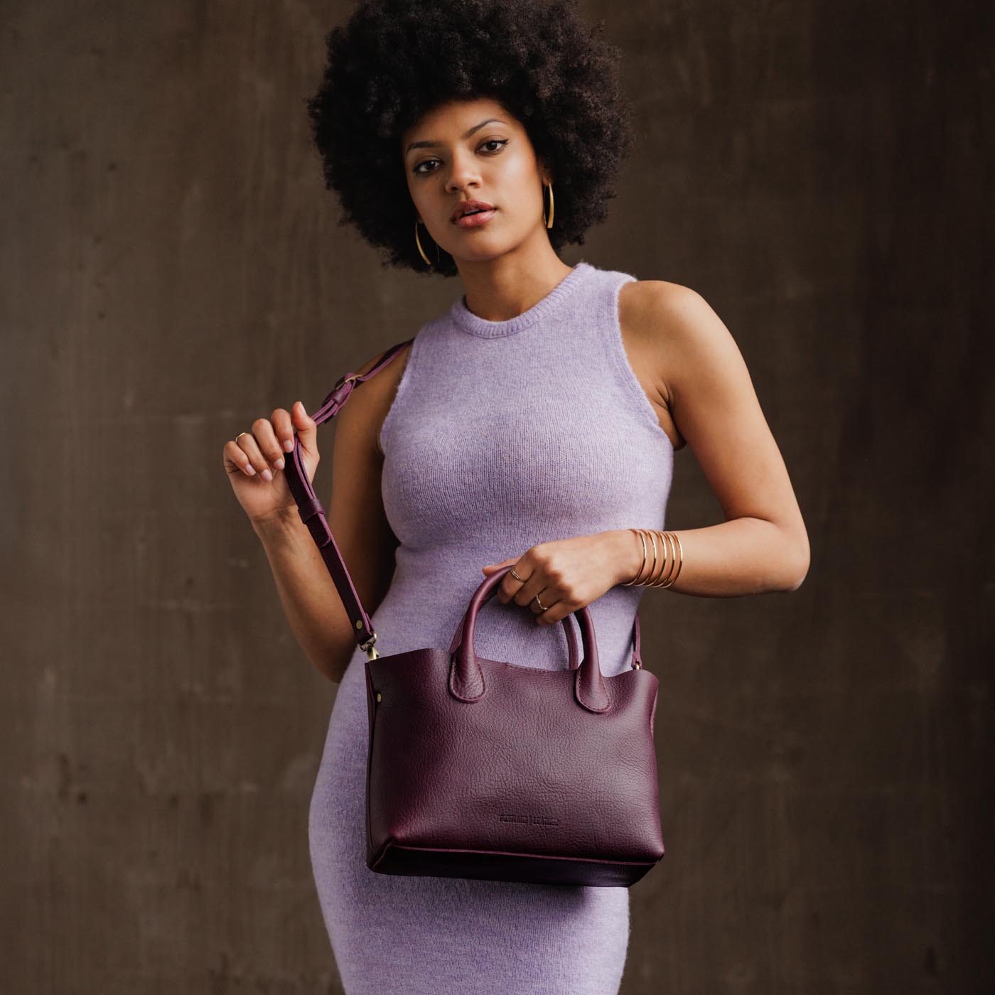 Plum*Large | Model holding mid-size tote purse with  structured leather handles and crossbody strap