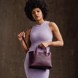 Plum Large | Model holding mid-size tote purse with  structured leather handles and crossbody strap