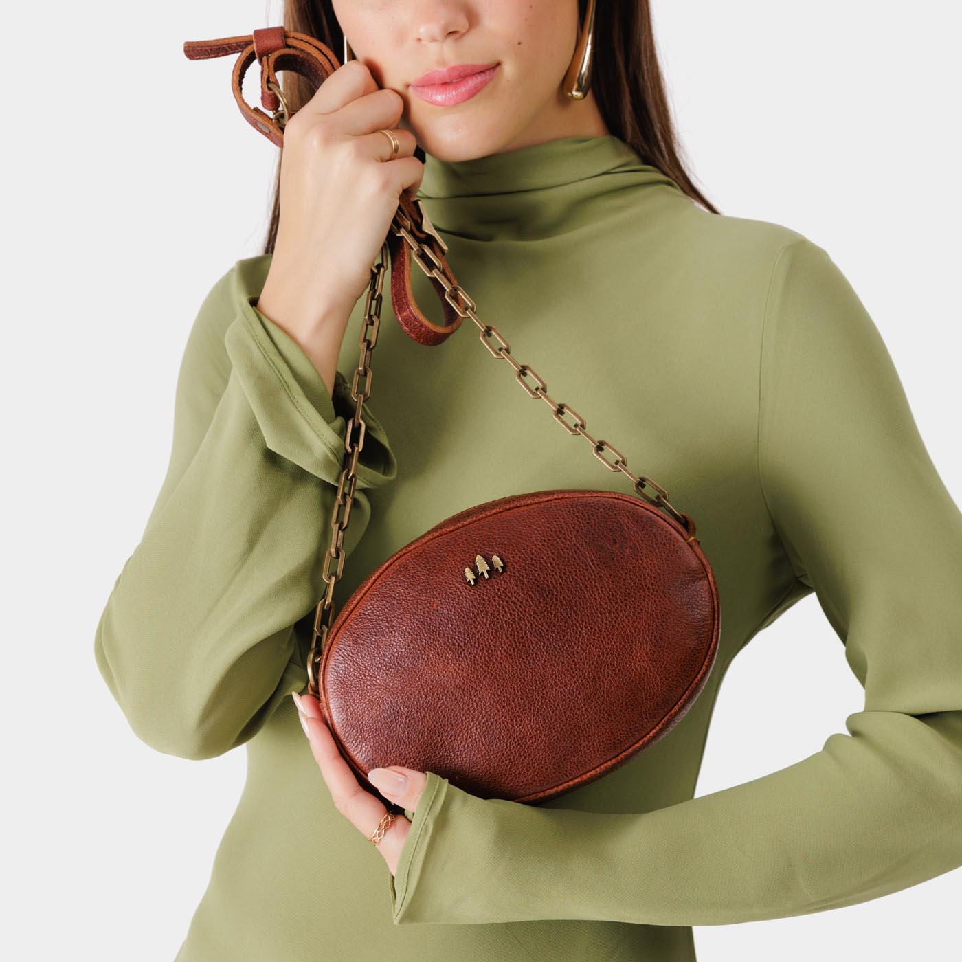 Nutmeg | Model holding oval leather purse with metal crossbody chain strap and adjustable leather shoulder guard