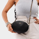 Pebbled--black | Model wearing oval leather purse with metal crossbody chain strap and adjustable leather shoulder guard