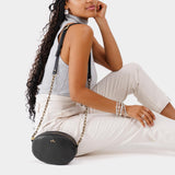 Pebbled--black | Model wearing oval leather purse with metal crossbody chain strap and adjustable leather shoulder guard