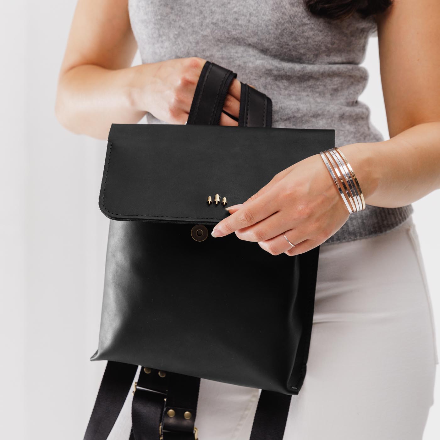 Black | Model holding rectangular backpack with leather lined nylon straps and magnetic flap closure