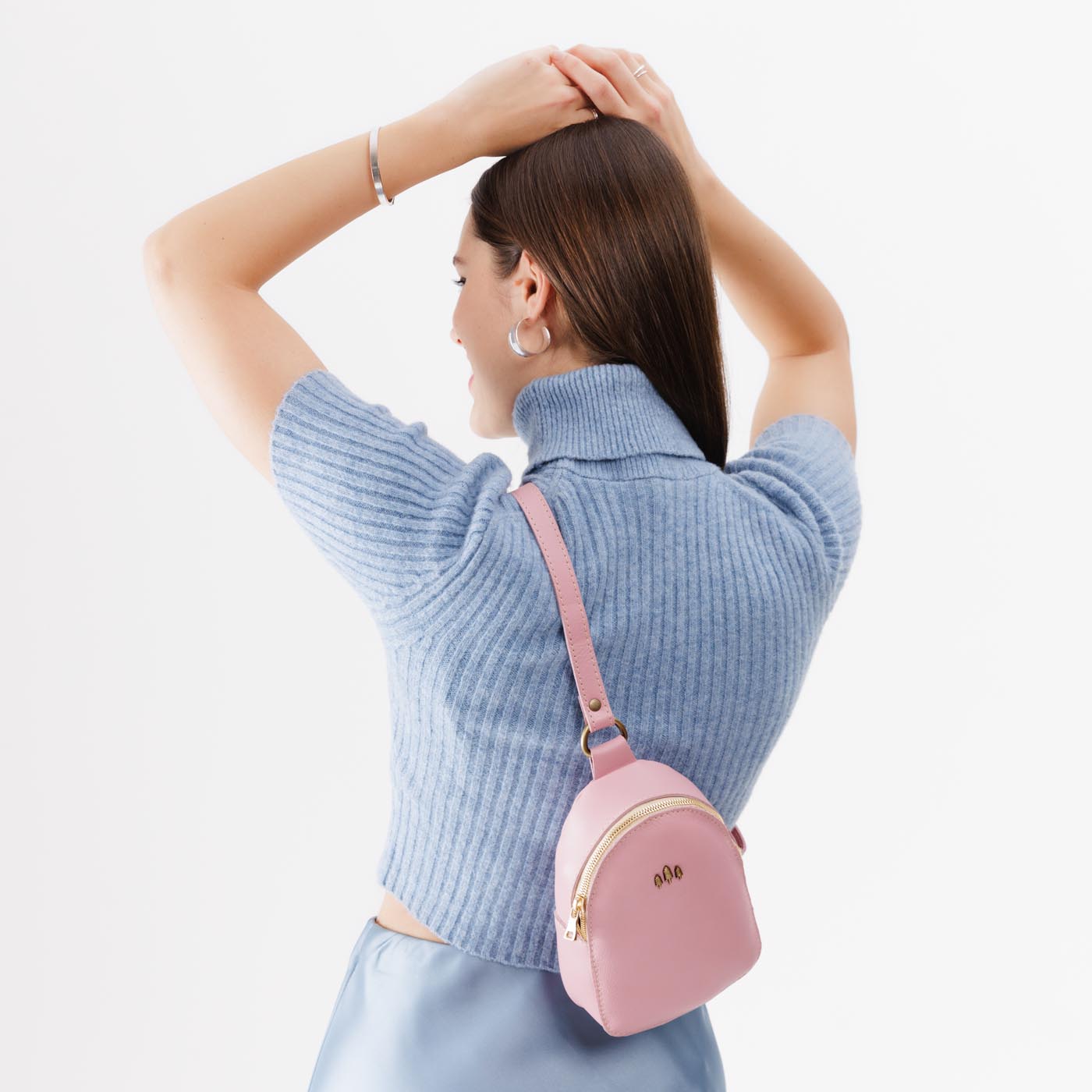 Vintage Pink | Model wearing small sling bag with zipper closure and adjustable strap on the back of her body