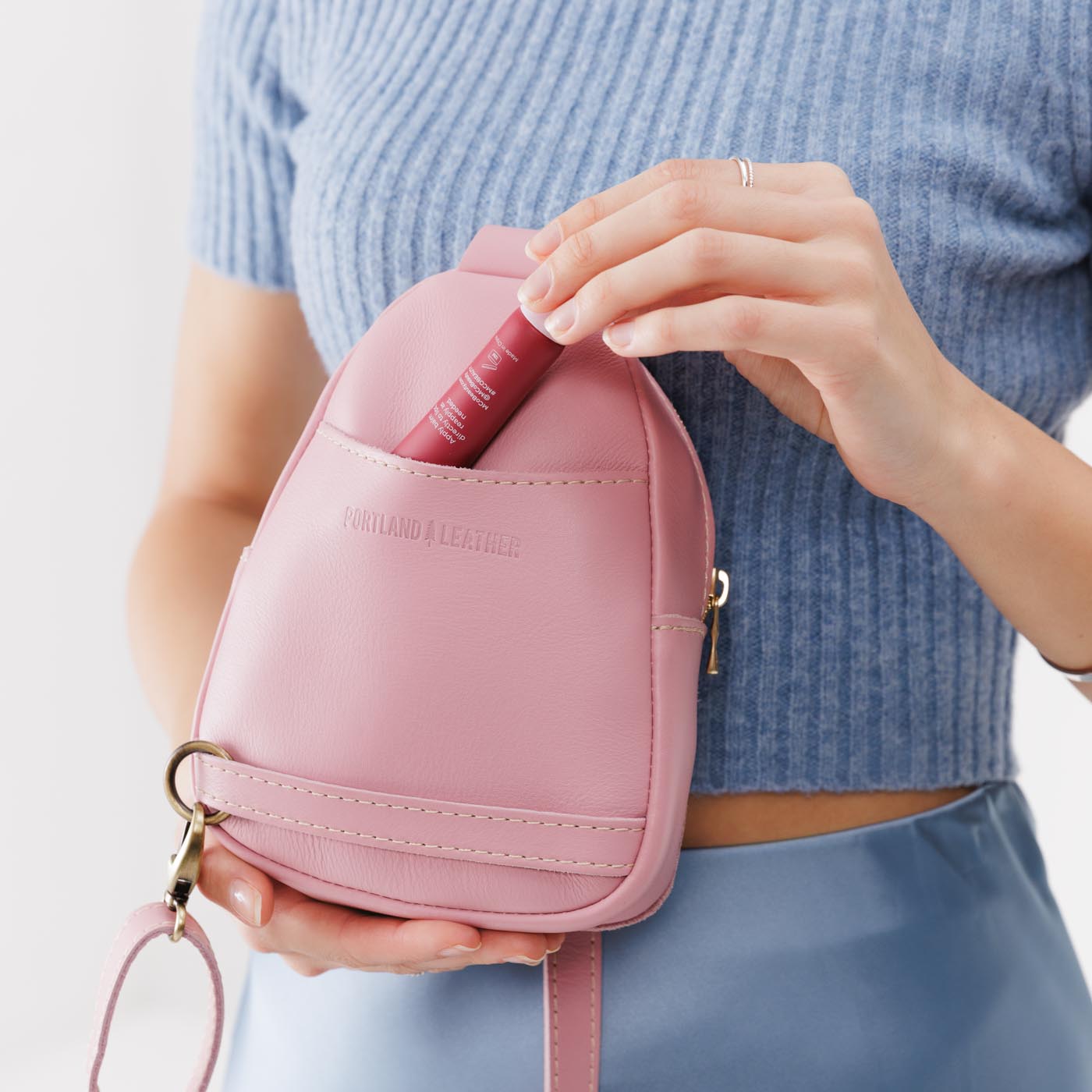 Vintage Pink | Model holding small sling bag with zipper closure and adjustable strap